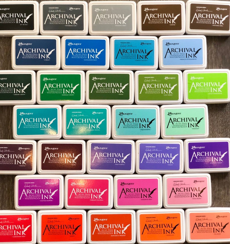 Peut inclure: Une collection de 36 tampons encreurs de diff&eacute;rentes couleurs. Chaque tampon porte l'inscription "Ranger Archival Ink" et est &eacute;tiquet&eacute; avec le nom de la couleur. Les tampons encreurs sont dispos&eacute;s en rang&eacute;es et en colonnes sur une surface en bois.