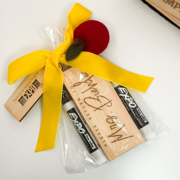 Könnte beinhalten: Eine Geschenktüte gefüllt mit Geschenken für Lehrer. Die Tasche enthält eine Holzplakette mit dem Text "Bitte zurückgeben an: Frau Biehl", zwei schwarze Trockenlöschmarker und einen roten Filzapfel.