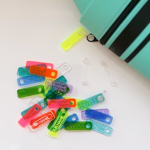 May include: Assortment of colorful plastic name tags with glitter and text that reads "Please return to [Your Name] Phone Number".