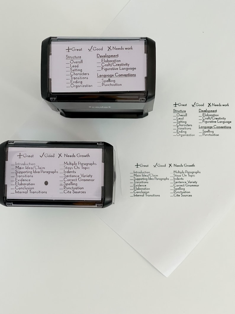 May include: Four black and white rubber stamps with different categories for grading writing. The categories include structure, development, introduction, main idea/claim, supporting idea paragraphs, transitions, evidence, elaboration, conclusion, internal transitions, multiple paragraphs, stays on topic, indents, sentence variety, correct grammar, spelling, punctuation, and cite sources.