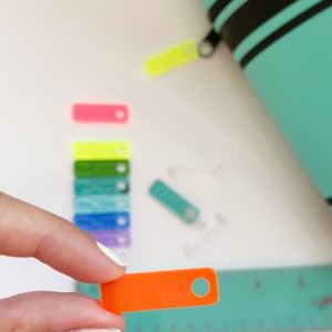 May include: An orange plastic tag with the text "Taylor Parsons" in white lettering. The tag has a hole in the top right corner.
