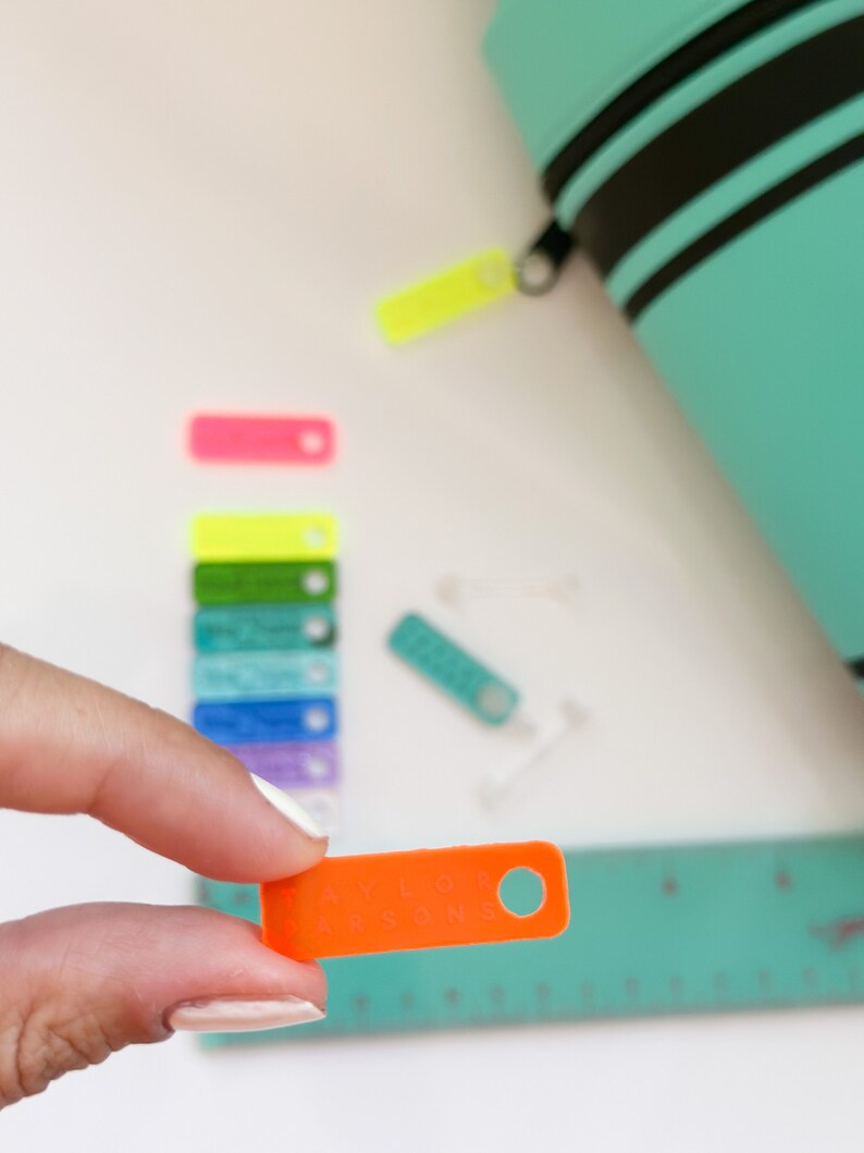 May include: An orange plastic tag with the text "Taylor Parsons" in white lettering. The tag has a hole in the top right corner.