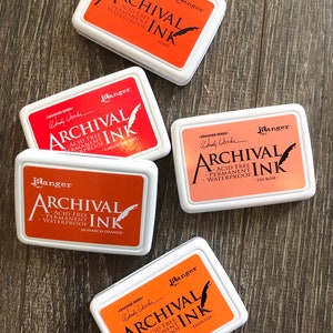 Peut inclure: Cinq tampons d'encre dans diff&eacute;rentes nuances d'orange et de rose. Chaque tampon est &eacute;tiquet&eacute; "Ranger Archival Ink" avec le nom de la couleur et "Sans acide, permanent, imperm&eacute;able".