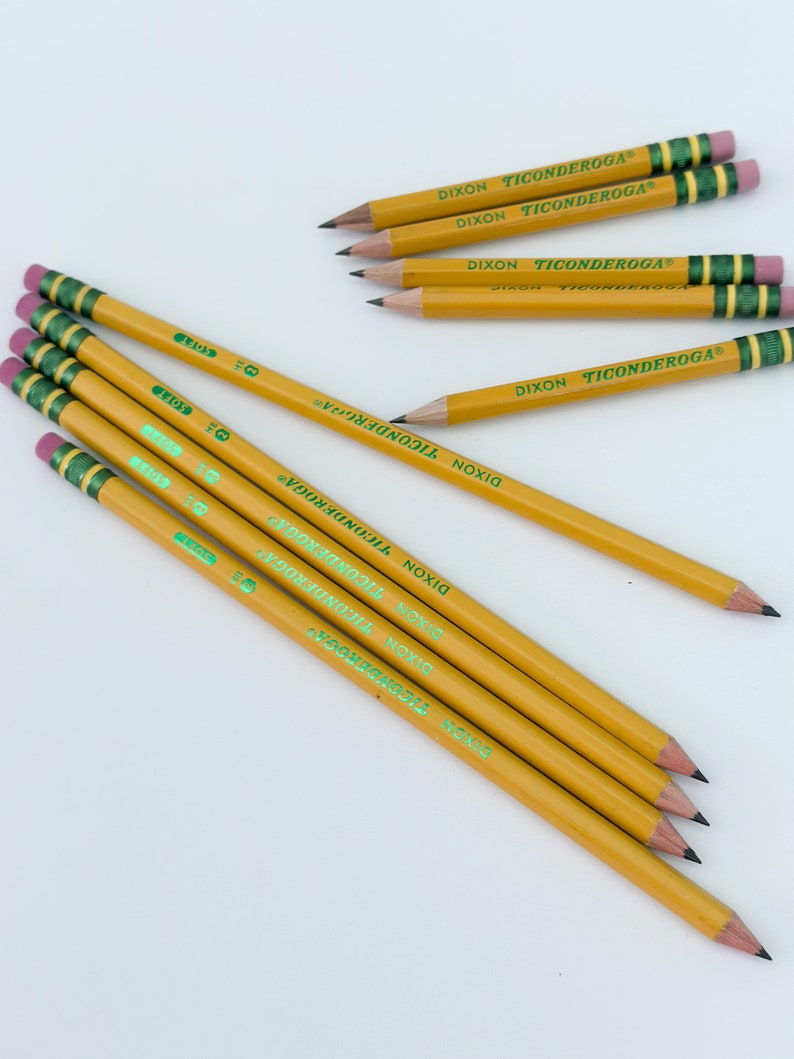 May include: A collection of yellow pencils with the text "DIXON TICONDEROGA" printed on the side. The pencils have green and gold bands near the eraser, and pink erasers. The pencils are arranged on a white surface.