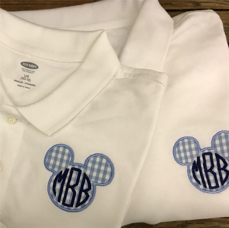 May include: Two white polo shirts with a blue and white gingham Mickey Mouse head design. Each head has the embroidered initials "MBB" in a dark blue color. The shirts are from Old Navy.