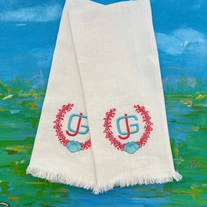 May include: Two white linen tea towels with frayed edges. Each towel features a coral reef design with a blue and green monogram in the center.