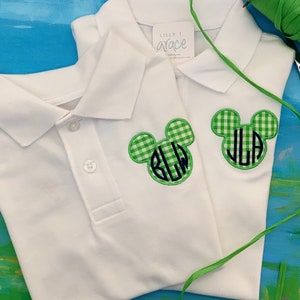 May include: Two white polo shirts with green and white gingham Mickey Mouse head patches. Each patch has a monogram in navy blue. The shirts have a button-down collar and the tag reads "Lilly T. Grace".
