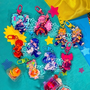 May include: A set of nine colorful anime character keychains with clear plastic backgrounds. Each keychain features a different character with a unique pose and expression. The keychains are attached to silver metal rings.