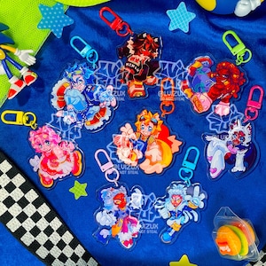 May include: Seven colourful keychains featuring cartoon characters with different designs. The keychains are made of clear plastic and have a metal ring for attaching to keys.