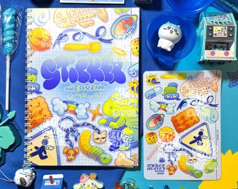 May include: A collection of colorful stickers, a spiral notebook, and various small toys arranged on a blue surface. The notebook features the text "Sticker Heaven" in a bubble font. Other items include a blue lollipop, a small arcade game, and a milk carton.