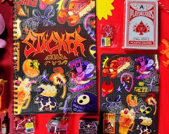 May include: A spiral-bound notebook and sticker sheets with colorful illustrations and the word "STICKER" in bold letters. A deck of playing cards, a yellow starburst, and other small items are arranged on a red surface.