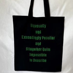 May include: Black canvas tote bag with green glitter text that reads "Unusually and Exceedingly Peculiar and Altogether Quite Impossible to Describe"