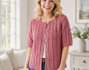 Könnte beinhalten: Eine altrosa Strickjacke mit kurzen Ärmeln, strukturiertem Zopfmuster, Rundhalsausschnitt und einer Knopfleiste auf der Vorderseite mit passenden runden Knöpfen. Das Kleidungsstück wird über einem weißen Oberteil und einer blauen Jeans getragen.