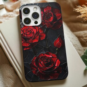 Pu&ograve; includere: Una custodia per telefono nera con un design di rose rosse su uno sfondo scuro. La custodia ha un ritaglio per l'obiettivo della fotocamera.