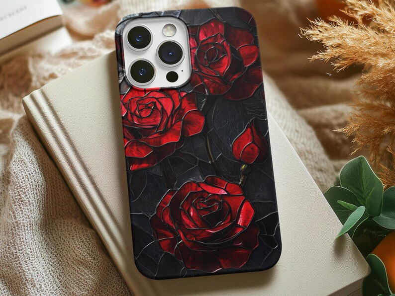 Pu&ograve; includere: Una custodia per telefono nera con un design di rose rosse su uno sfondo scuro. La custodia ha un ritaglio per l'obiettivo della fotocamera.