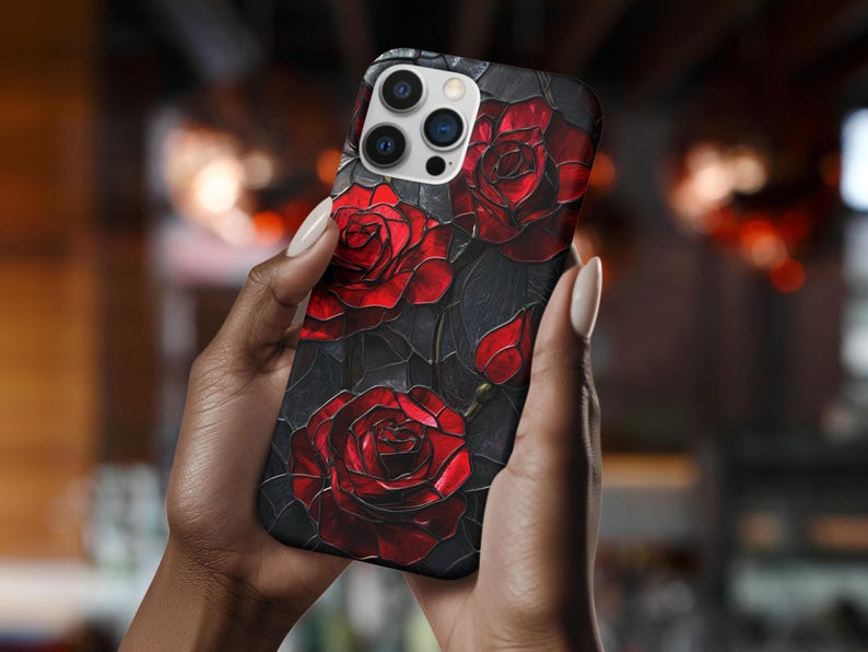 Pu&ograve; includere: Una custodia per telefono nera con un design di rose rosse su uno sfondo scuro. La custodia ha un ritaglio per l'obiettivo della fotocamera e un bordo nero.