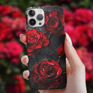 Pu&ograve; includere: Una custodia per telefono nera con un design di rose rosse su uno sfondo scuro. La custodia ha un ritaglio per l'obiettivo della fotocamera e un design elegante e moderno.