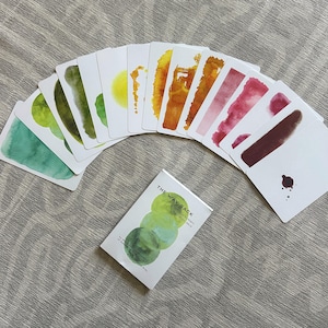 May include: A deck of cards titled THE WAY BACK, featuring a white box with three overlapping green watercolor circles. The cards are fanned out, displaying various abstract watercolor strokes in shades of green, yellow, orange, red, and brown.
