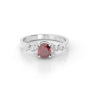 Op de afbeelding: Een zilveren ring met een rode edelsteen omringd door kleinere witte edelstenen.