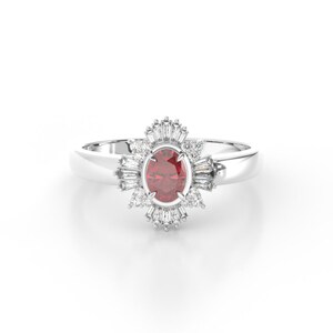 May include: A silver ring with a red oval gemstone surrounded by a halo of smaller white gemstones.
