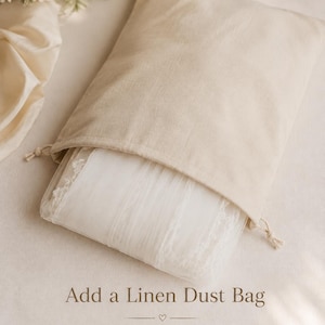 May include: A beige linen drawstring dust bag containing a folded white lace-trimmed veil. The text on the image reads: Add a Linen Dust Bag to safely store and protect your veil before and after wedding.