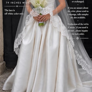 May include: An off-white veil measuring 138 inches long and 79 inches wide, featuring intricate lace trim along the edges. The veil is worn over a solid off-white strapless gown, and the lace is off-white. Text includes OFF-WHITE VEIL.