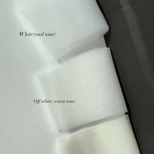 May include: A close-up of three fabric swatches in shades of white. The top swatch is labelled "White (cool tone)", the middle swatch is "Off white (warm tone)", and the bottom swatch is "Ivory". The fabrics are layered and folded.