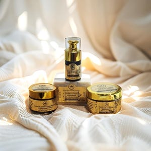 May include: A collection of skincare products with gold and black packaging. The set includes a serum, two jars of cream, and a bar of soap. The labels feature text in multiple languages. The products are arranged on a white, textured surface.