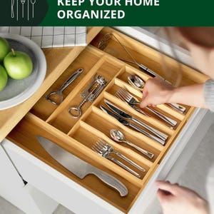 Puede incluir: Un organizador de cajones de bambú lleno de cubiertos y utensilios de cocina. El cajón está abierto, revelando un cuchillo, tenedores, cucharas y otras herramientas. El texto "KEEP YOUR HOME ORGANIZED" está en la parte superior.