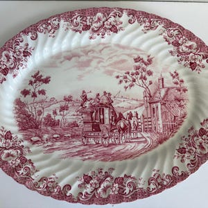 May include: An oval ceramic serving platter featuring a white base with a deep red transferware pattern. The center depicts a horse-drawn stagecoach on a country road, while the scalloped rim is decorated with intricate floral scrollwork.