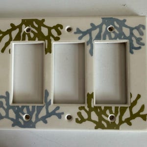 May include: A rectangular off-white triple light switch wall plate featuring a repeating pattern of olive green and light blue coral-like branch silhouettes. The plate includes three rectangular cutouts and four screw holes for installation.