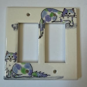 Può includere: Copri interruttore doppio color crema con illustrazioni di gatti dipinte a mano. I gatti hanno macchie blu, verdi e viola. La copertura ha una finitura lucida ed è progettata per interruttori standard.