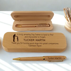 May include: A wooden pen and case set. The pen is light brown with gold accents and the name "Tucker Martin" engraved on it. The wooden case has a hinged lid and a personalized message for a dog trainer.