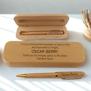 May include: A wooden pen and case set with gold detailing. The pen is engraved with "Oscar Berry." The case is engraved with a message: "A truly amazing Web developer is hard to find and impossible to forget. OSCAR BERRY. Thank you for bringing ideas to life online. Kathleen Payne."