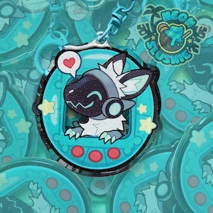 May include: A teal and black glittery keychain featuring a cartoon protogen character with a heart speech bubble. The keychain has a teal frame with red circles at the bottom and yellow star accents. The text "Neon Slushie" is visible.