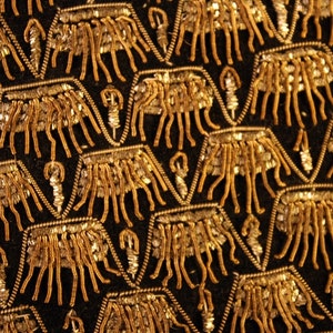 May include: Close-up of a black fabric with a repeating pattern of gold embroidered geometric shapes.