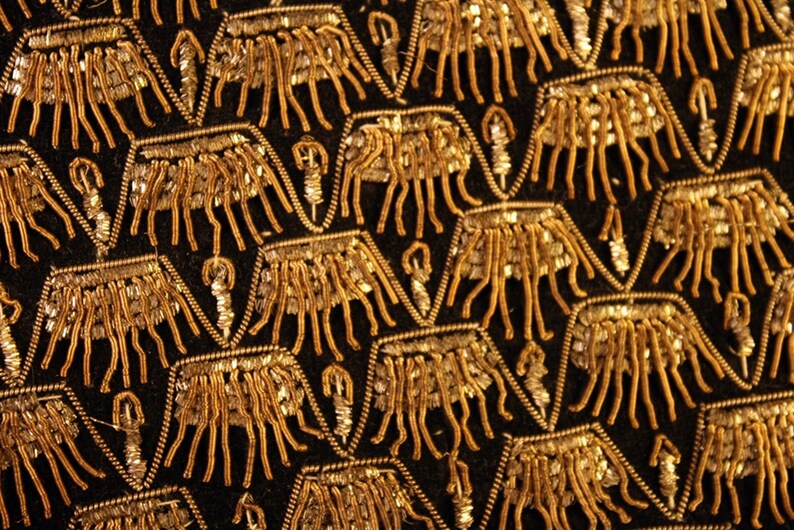 May include: Close-up of a black fabric with a repeating pattern of gold embroidered geometric shapes.
