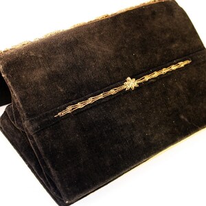 May include: A black velvet clutch with gold embroidery. The clutch has a flap closure and a decorative gold trim.