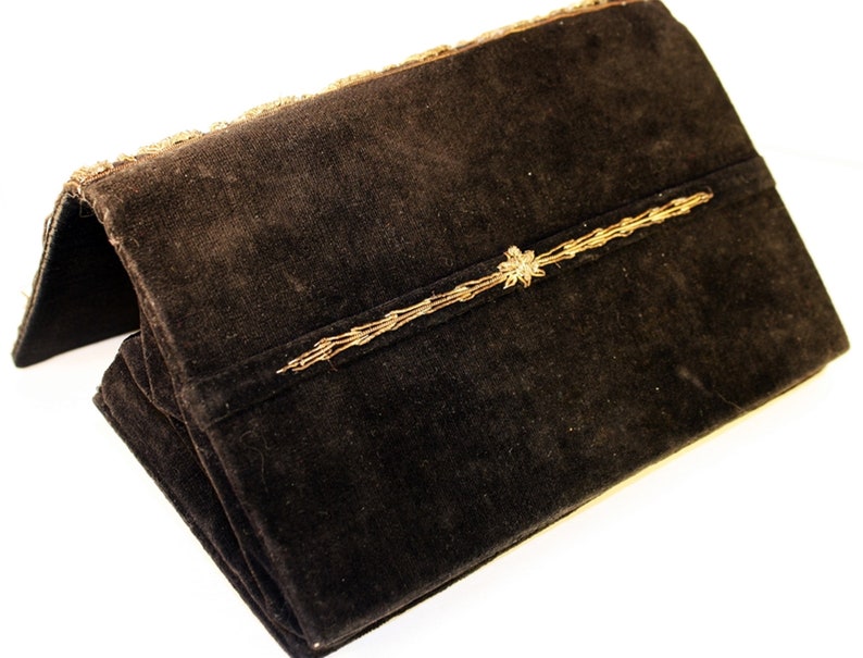 May include: A black velvet clutch with gold embroidery. The clutch has a flap closure and a decorative gold trim.