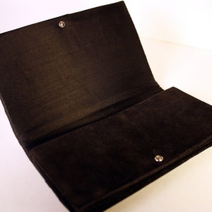May include: A black velvet clutch bag with a snap closure and a silver button.