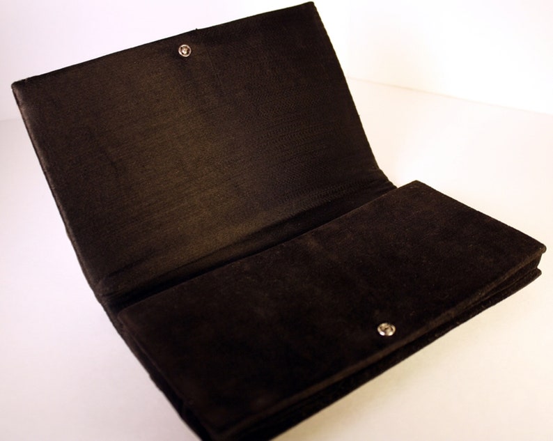 May include: A black velvet clutch bag with a snap closure and a silver button.