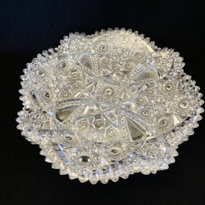 May include: A clear glass bowl with a cut glass design. The bowl has a scalloped edge and a starburst pattern.