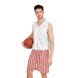May include: A white sleeveless basketball jersey with a V-neck, paired with red and white striped shorts. The person is holding a brown basketball. The outfit is designed for sports and athletic activities.