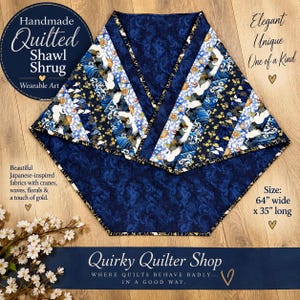 May include: A quilted shawl shrug featuring a dark blue fabric with a tonal floral pattern and diagonal panels of fabric printed with white cranes, blue waves, and gold floral accents. The garment measures 64 inches wide by 35 inches long.