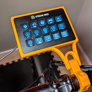 Peut inclure: Un Stream Deck noir avec un cadre jaune et une variété de boutons avec des lumières bleues. Le Stream Deck est monté sur un guidon de vélo noir.