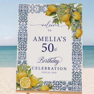 May include: A rectangular welcome sign for Amelia's 50th Birthday Celebration on July 25, 2028. The sign features a blue and white tile pattern border, yellow lemon illustrations with green leaves, and dark blue text on a cream background.