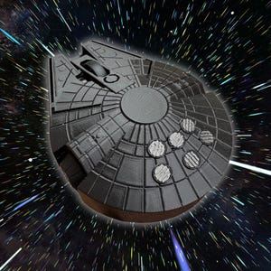 May include: A black 3D printed model of the Millennium Falcon spaceship from Star Wars. The model is detailed with a textured surface and features a round cockpit and a rear engine.