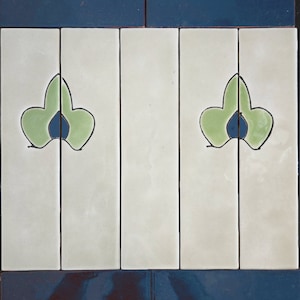 May include: A set of four white ceramic tiles with a blue border and a green leaf design. The leaves are stylized and have a blue center.