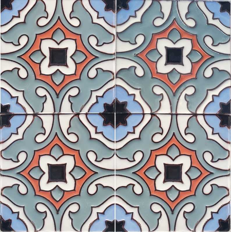 Op de afbeelding: Vier vierkante keramische tegels die samen zijn gerangschikt en een herhalend patroon vertonen. Het ontwerp omvat een centrale oranje bloemvorm met een zwart vierkant midden, omgeven door witte, blauwe en blauwgroene accenten. De tegels hebben een glanzende afwerking.