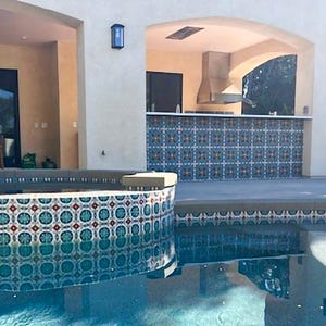 May include: An outdoor living space with a swimming pool and a built-in bar area. The pool has a decorative tile border. The bar features a tiled backsplash and a stainless steel range hood. The architecture is a light beige color.